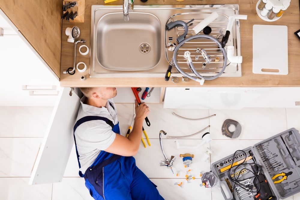 A plumber is fixing a sink in a kitchen.