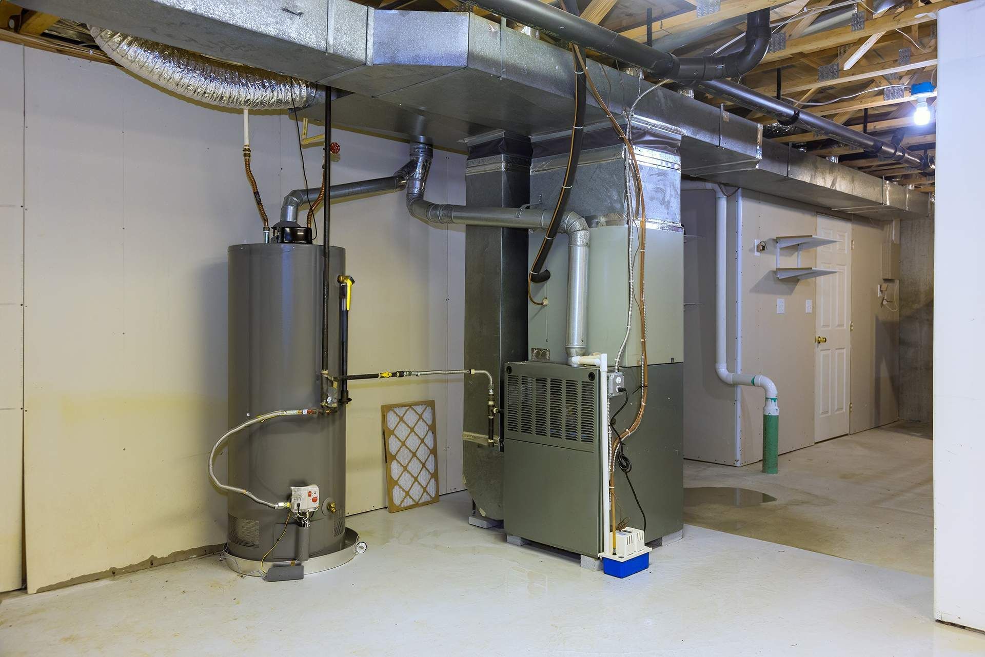 Water heater and furnace in a basement. Gray appliances against light walls.
